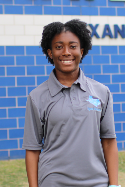 India Thomas with a bright smile stands in front of a blue brick wall.