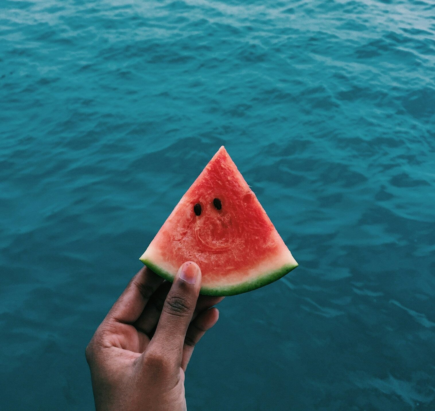 person holding sliced watermelon near body of water