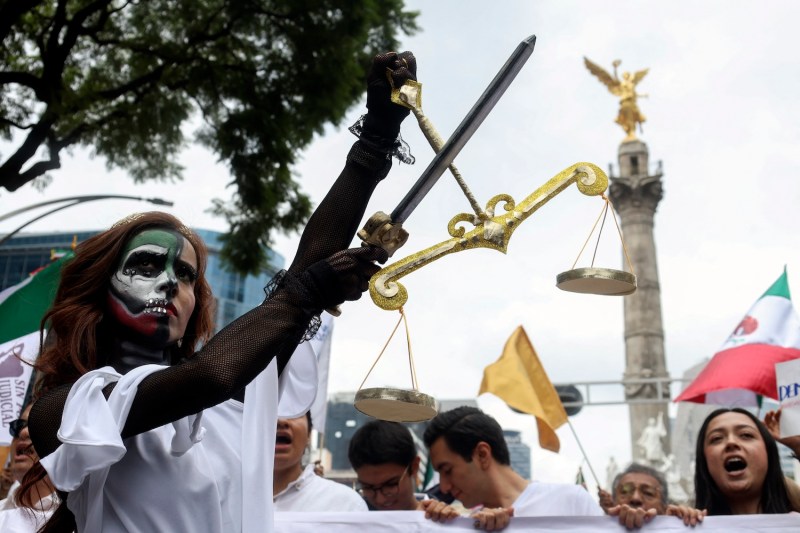 A young woman dressed as Lady Justice, carrying a sword and a set of scales, takes part in a protest in Mexico City.