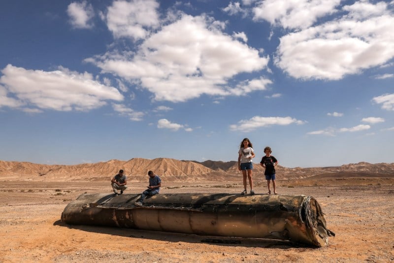 People stand on top of the remains of an Iranian missile in the Negev desert in the aftermath of an Iranian missile attack on Israel.