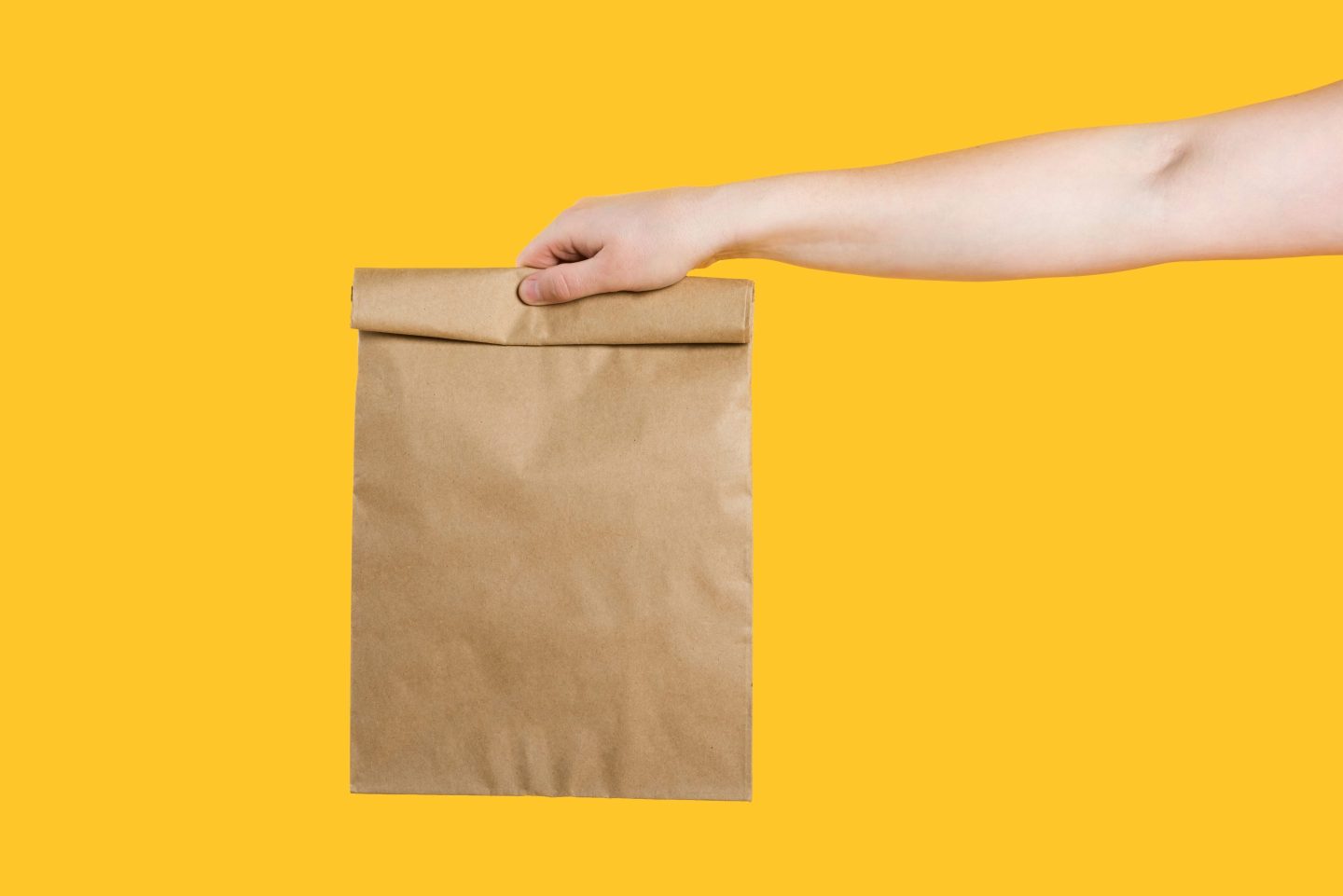 An outstretched arm holding a brown paper bag