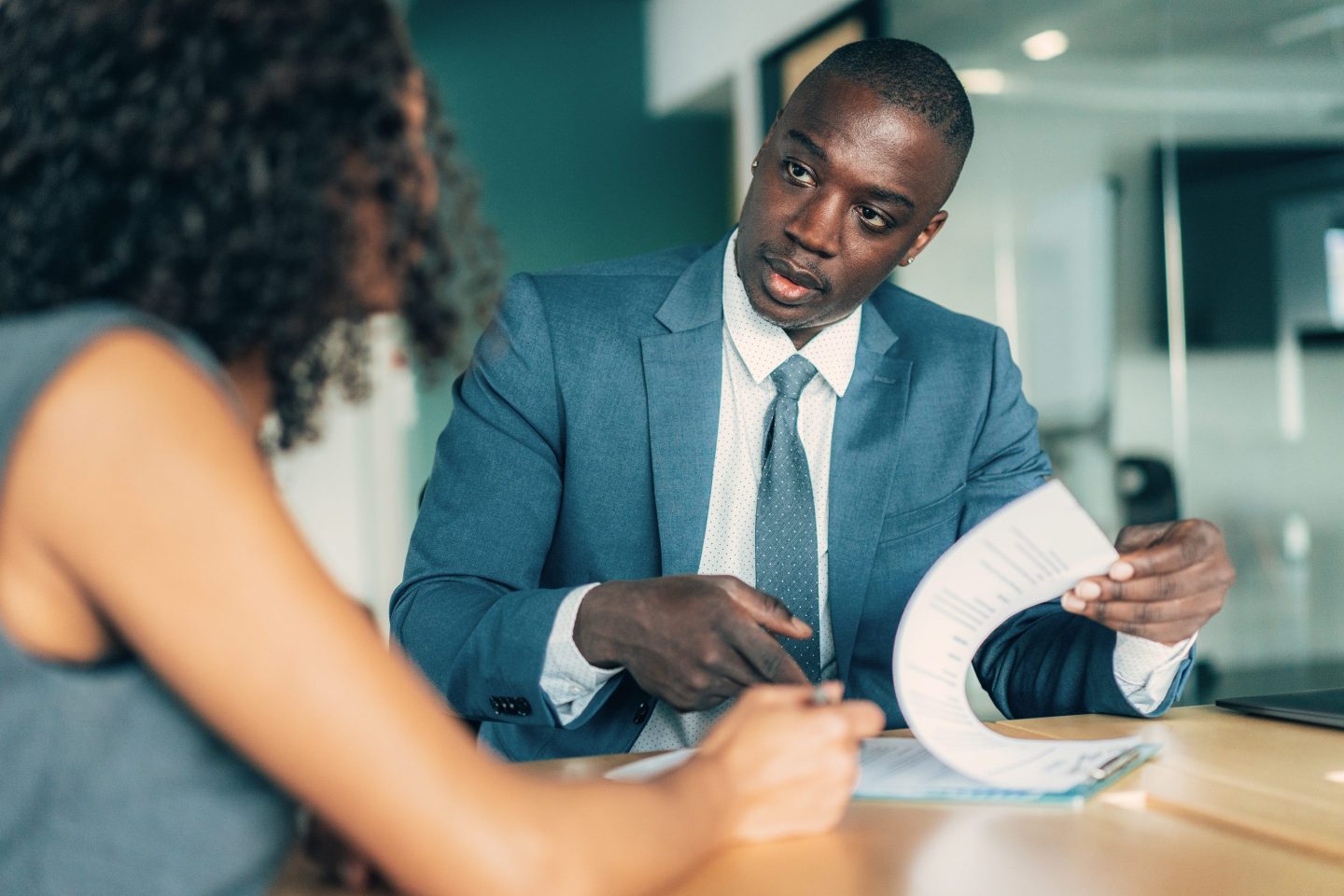 A person pointing at forms on a clipboard in a business meeting.