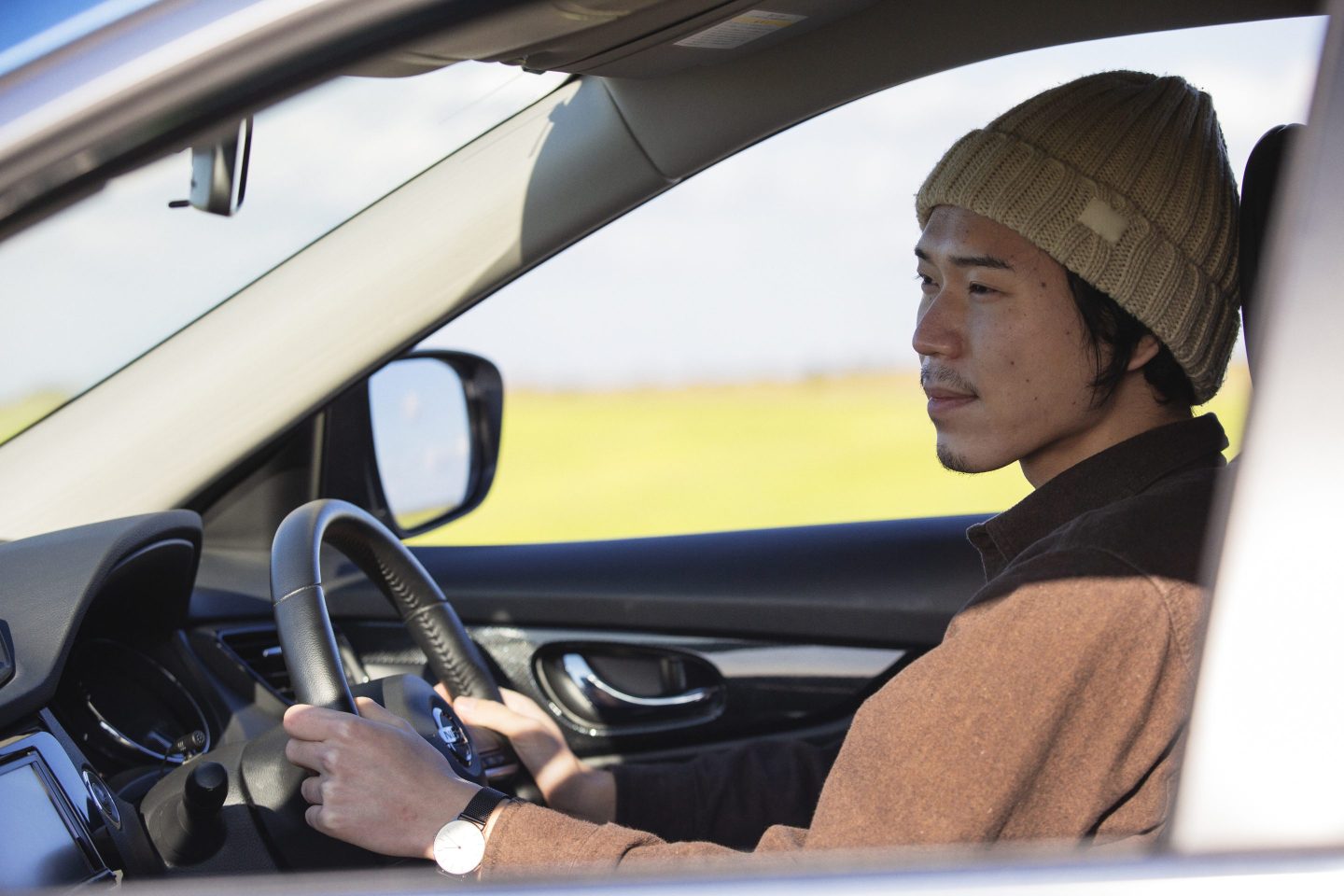 A man behind the steering wheel of a car looks out the window.