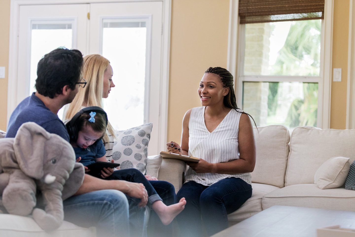 A social worker sitting on a couch with a notepad, smiling at a family consisting of a mother, father, and daughter seated across from her.