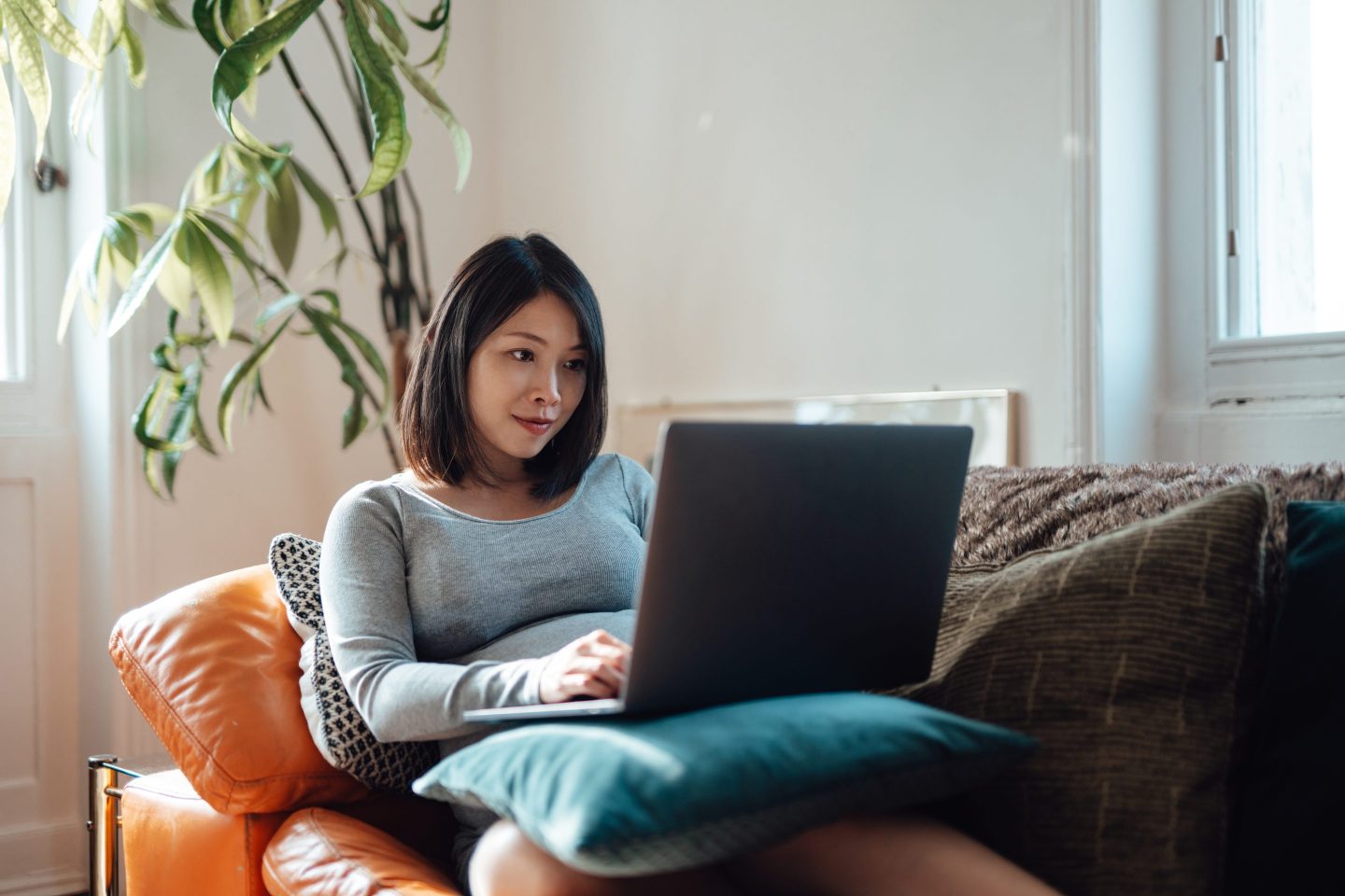 Young pregnant businesswoman at home office, working with laptop on sofa