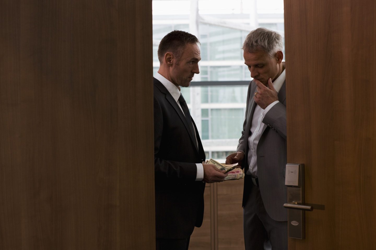 Two businessmen in the shadows doing a transaction