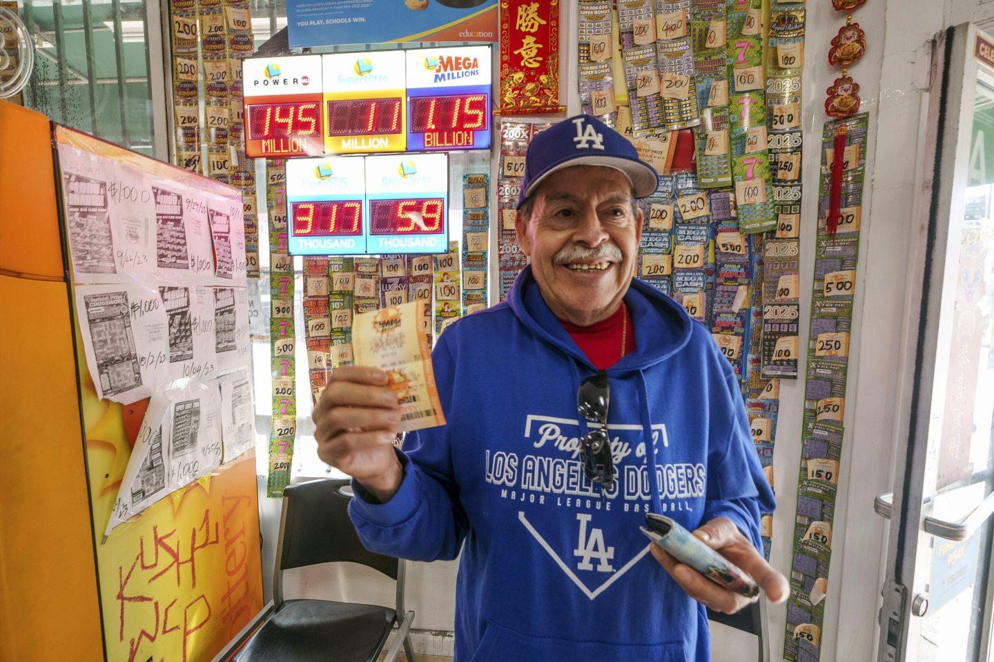 A man wearing Dodgers apparel stands with a Mega Millions lottery ticket he purchased from a convenience store