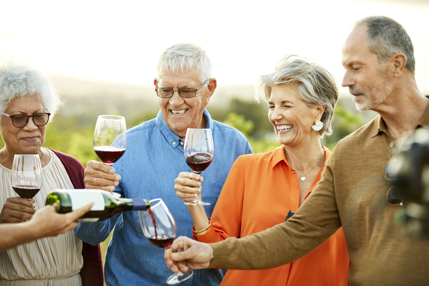 Man pouring wine for females and males in vineyard.