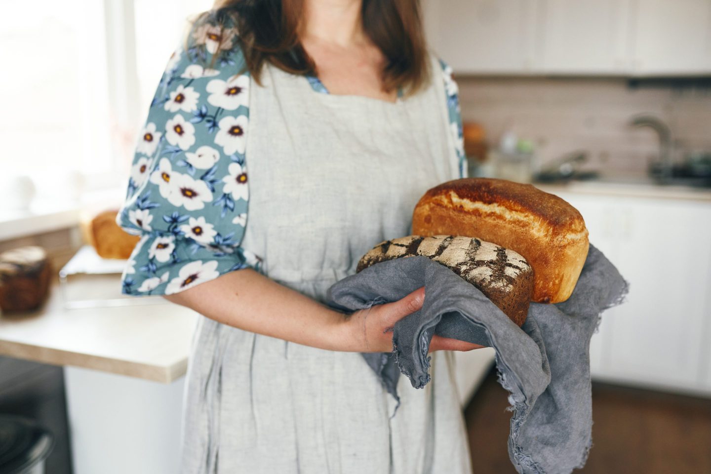 An unidentified woman holds a ready-baked bread in her hands on a linen napkin