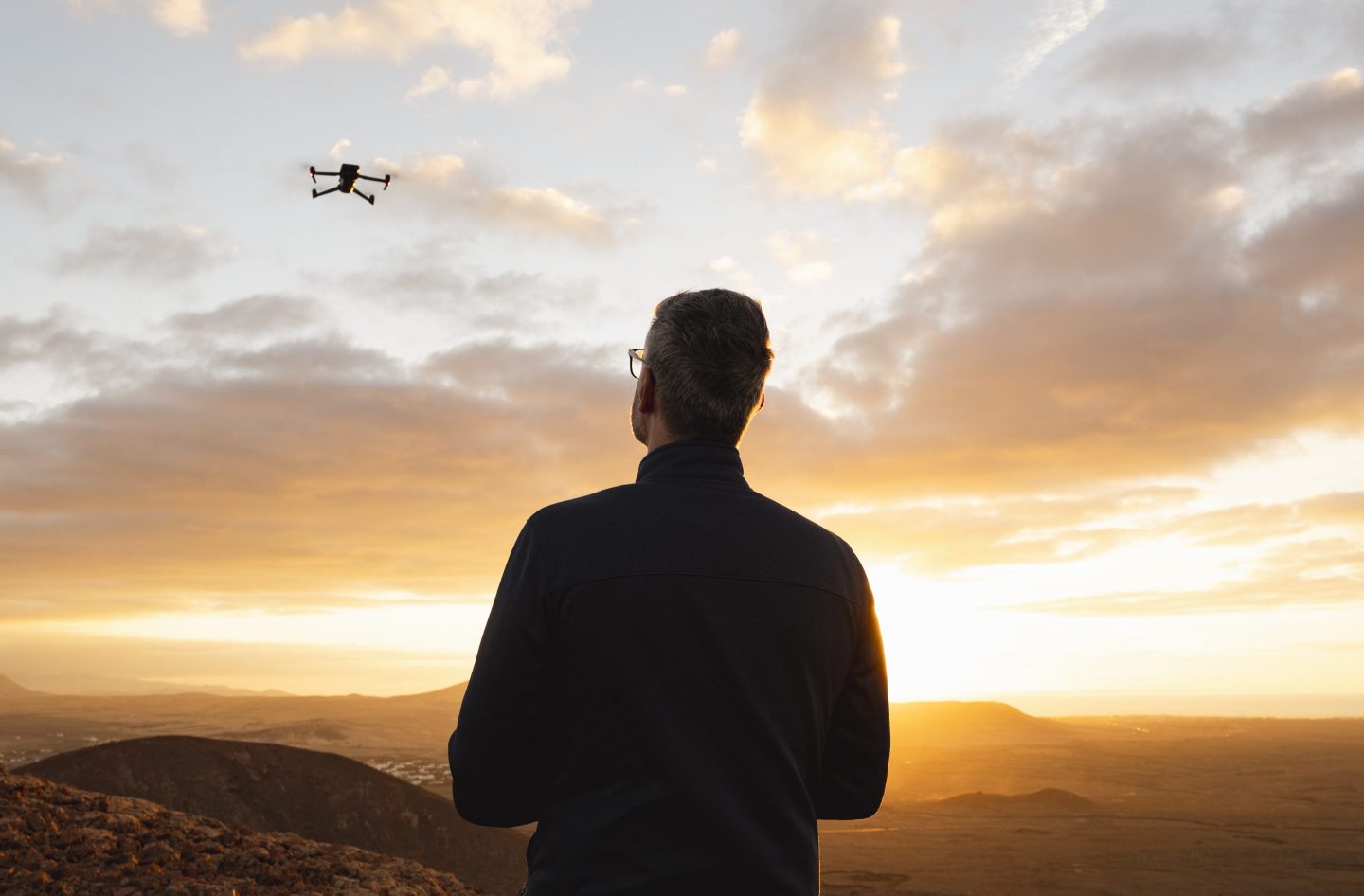 Spain, Canary Islands, Fuerteventura, Calderon Hondo, mature male standing on the edge of a volcano flying a drone