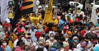 Imagem de manifestação contra a opressão direcionada à população negra. Há bandeiras de movimentos sociais, como a Unegro. Há também pessoas usando roupas relativas a cultos de matriz africana. Todas as pessoas na imagem usam máscaras para proteção contra o vírus Sars O ato reforça a lógica segundo a qual vidas negras importam.-CoV-2.