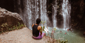 A woman sits on a rock overlooking a waterfall.