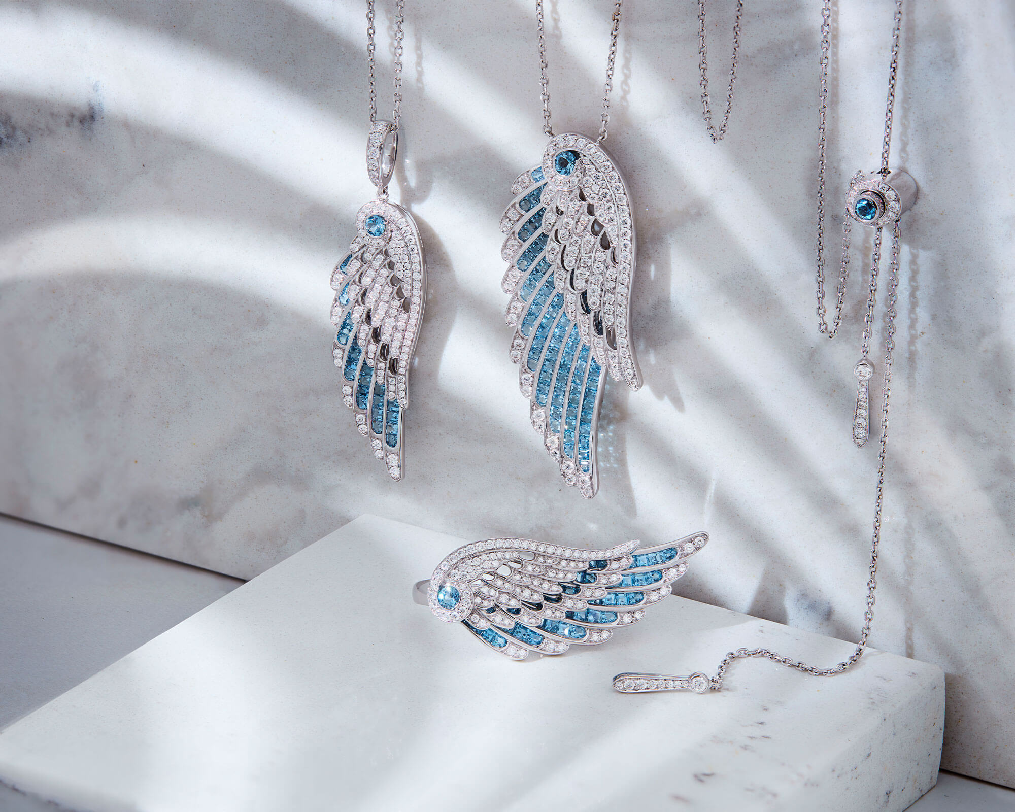 Close up of a Wings Jewellery collection aquamarine and diamond bangle pendants and ring from Garrard marble