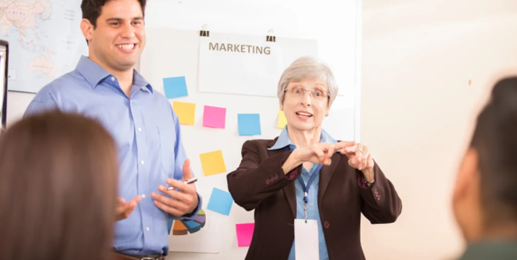 Two persons standing in front of a room communicating through sign language