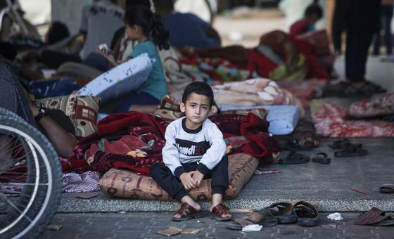 A five-year-old boy sits on his mattress in a shelter courtyard surrounded by several hundred other displaced people.