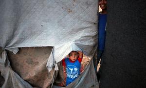 A young child peers through the ripped side of a shelter in the Gaza Strip.