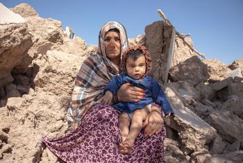 A woman holds a 6-month-old child while sitting in rubble of homes in Afghanistan which were destroyed by an earthquake.