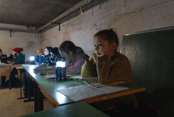 Children in Borodianka, Ukraine, study under lamplight in a shelter.