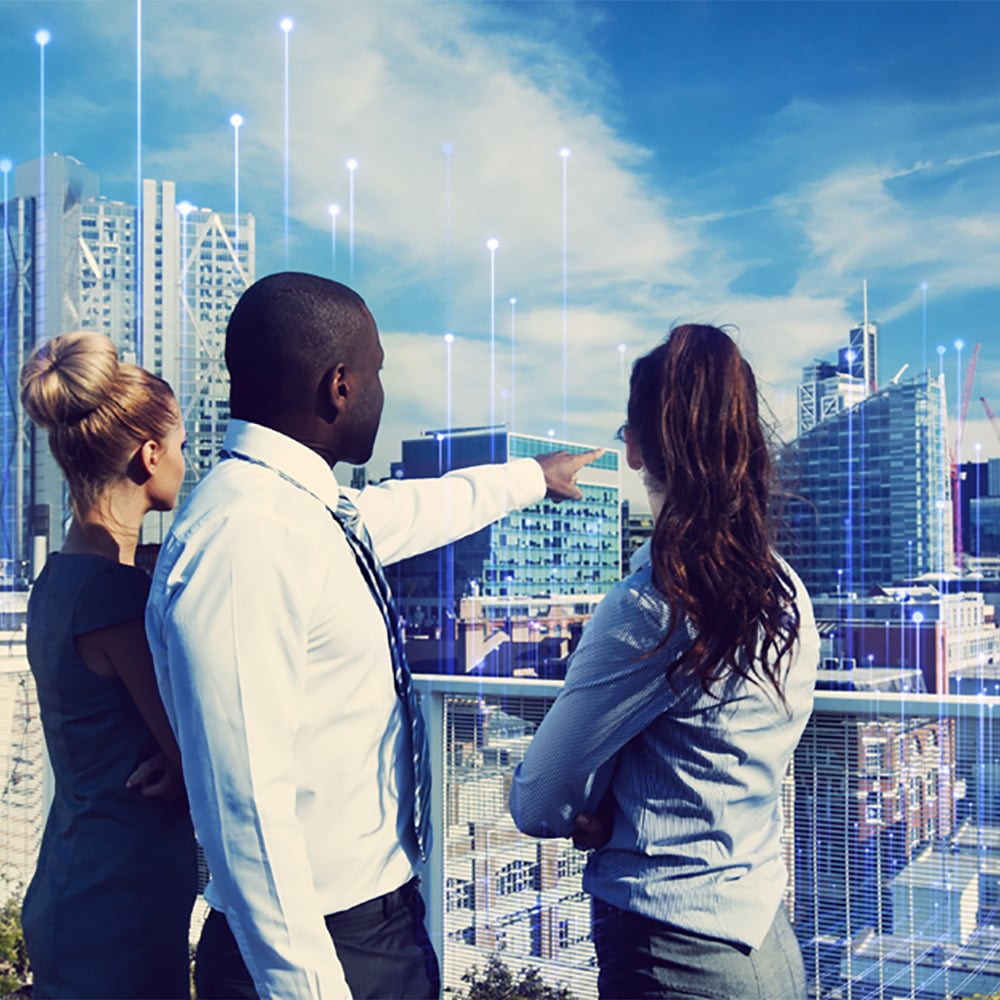 People in an office building look out a large window and point to the city