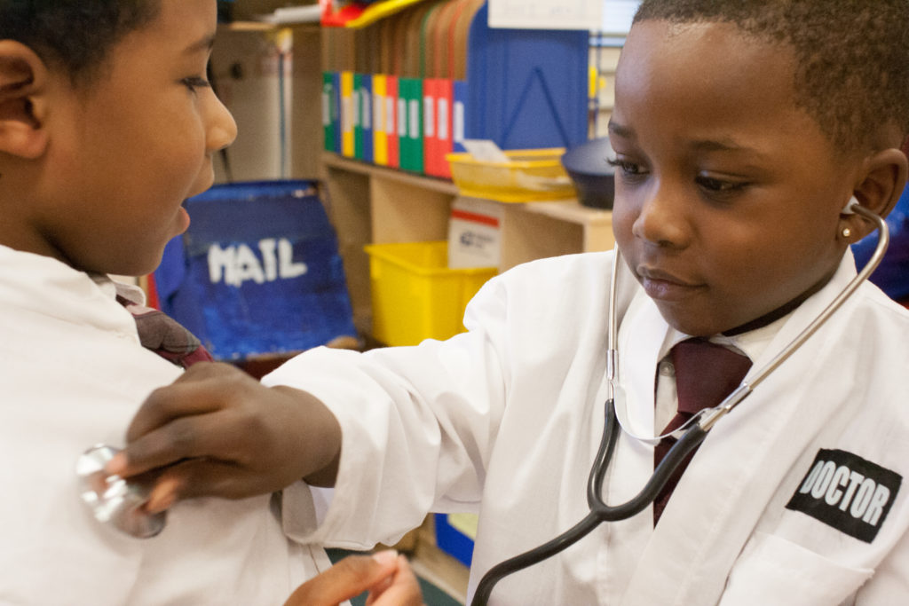 Healthy Harlem | A little boy dressed as a doctor playfully holds a stethoscope to another boy.