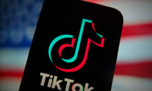 An phone displaying the TikTok logo in front of a blurry American flag. 