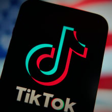 An phone displaying the TikTok logo in front of a blurry American flag. 