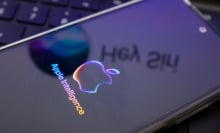 The Apple Intelligence logo is being displayed on a smartphone, with the Apple Siri logo in the background