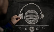 A person drawsingthe Spotify logo wearing a pair headphones in chalk. 