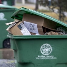 A green recycling bin with the city of Houston logo, full of cardboard boxes. 