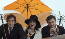 A trio of people shown from the waist up, holding umbrellas