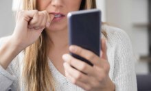 Woman looks at phone and bites her nail.