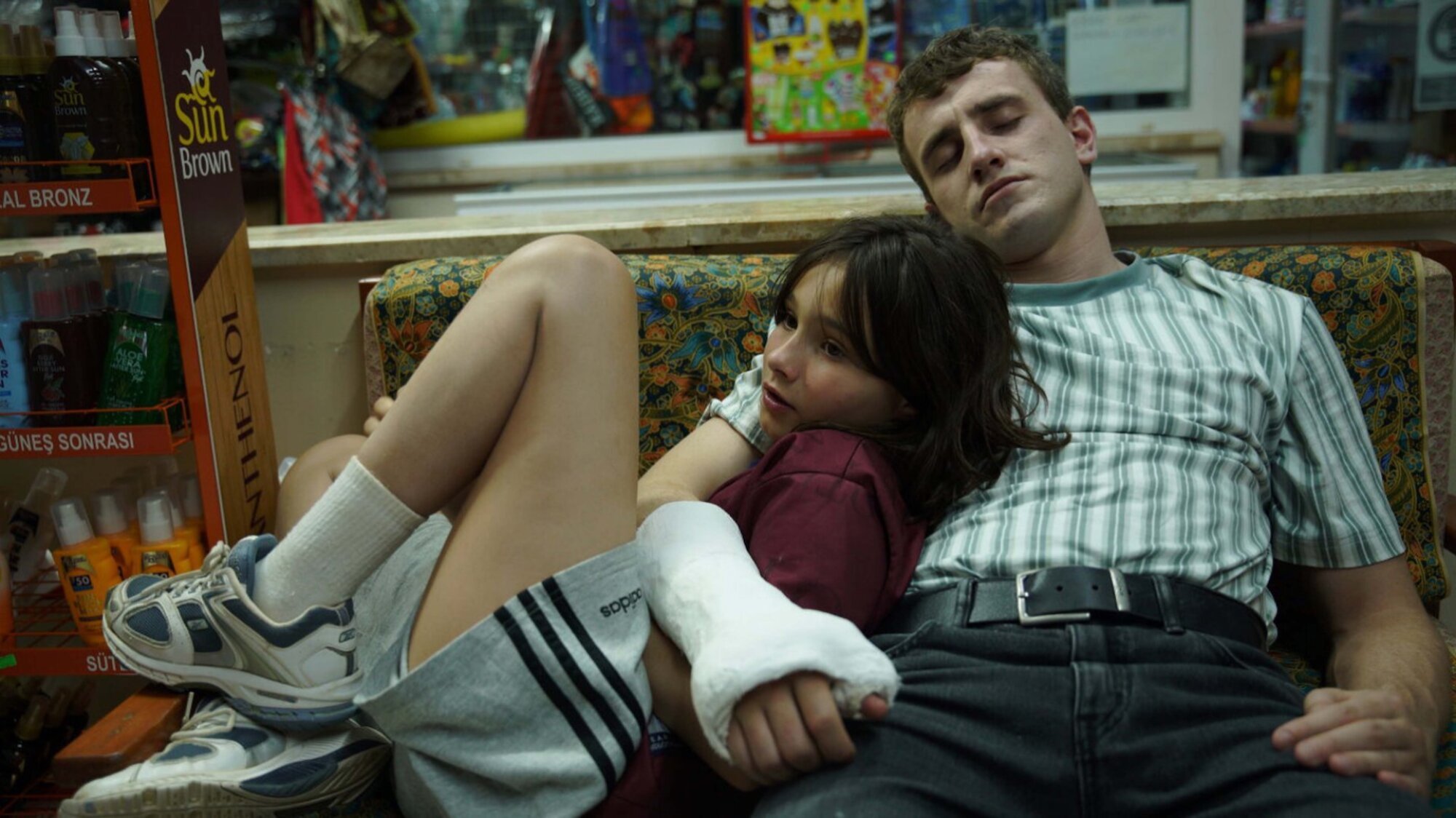 A father, with his eyes closed, leans back on a couch with arm, which is in a cast, around his daughter.