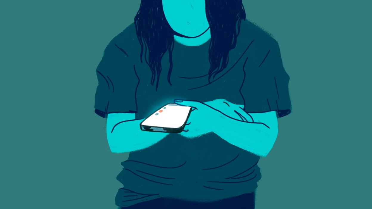 A woman looks down at her glowing phone.