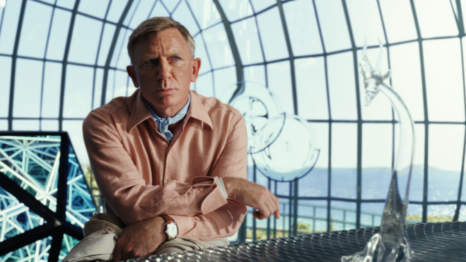 Man sits by a table with a large glass window behind him. 