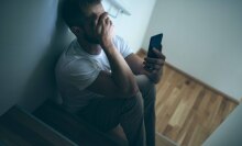 A man covers his face while holding his phone in his hand. 