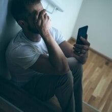 A man covers his face while holding his phone in his hand. 