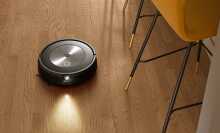 Roomba j7 robot vacuum cleaning hardwood floor with kitchen chair legs in peripherals