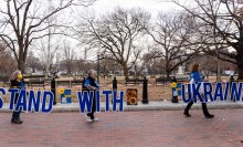 Three women carry a sign that reads Stand With Ukraine at the White House in Washington, D.C.