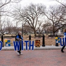 Three women carry a sign that reads Stand With Ukraine at the White House in Washington, D.C.