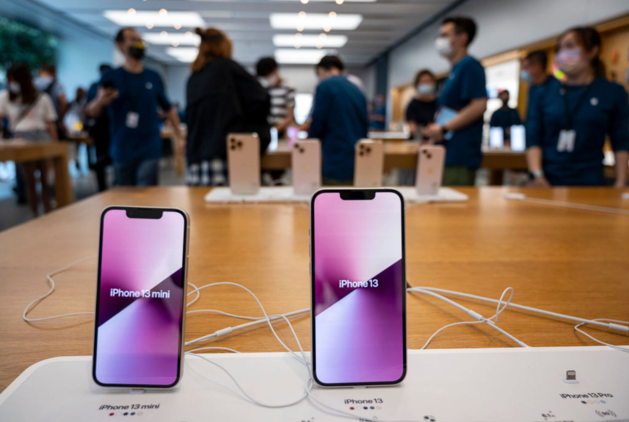 Two iPhones at the Apple store with their names on screen. iPhone 13 mini on left, iPhone 13 on right.