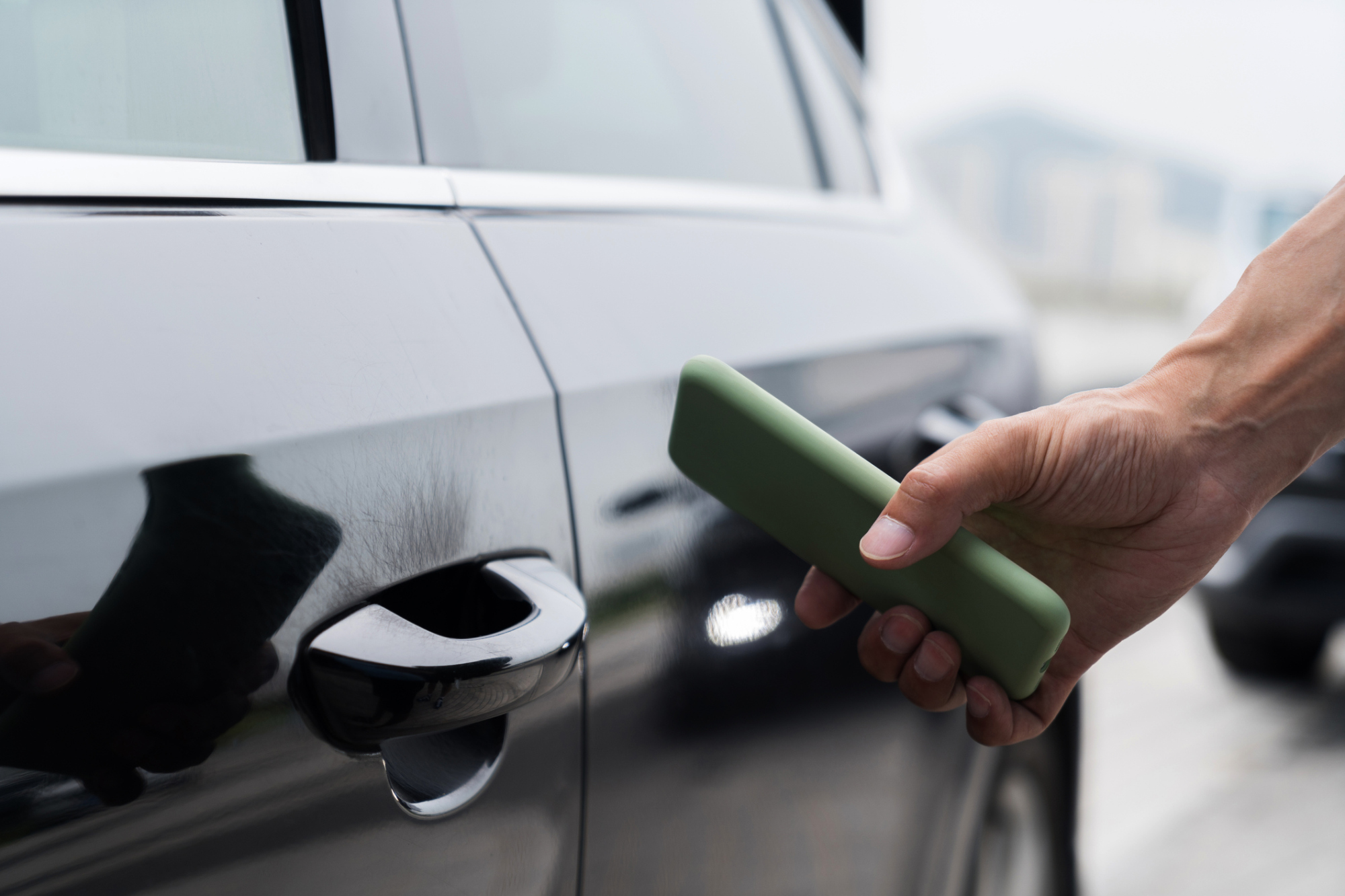 Black car with someone's hand nearby holding a green smartphone.