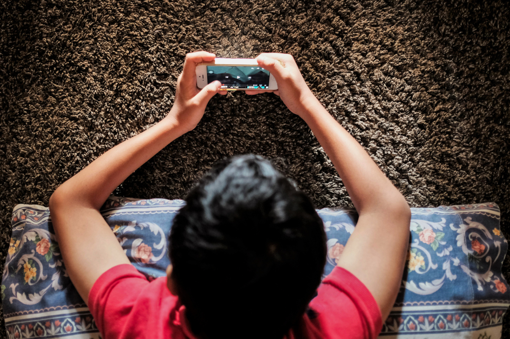 Back of a boy's head while he is playing games on his phone. Shot takeen overhead.