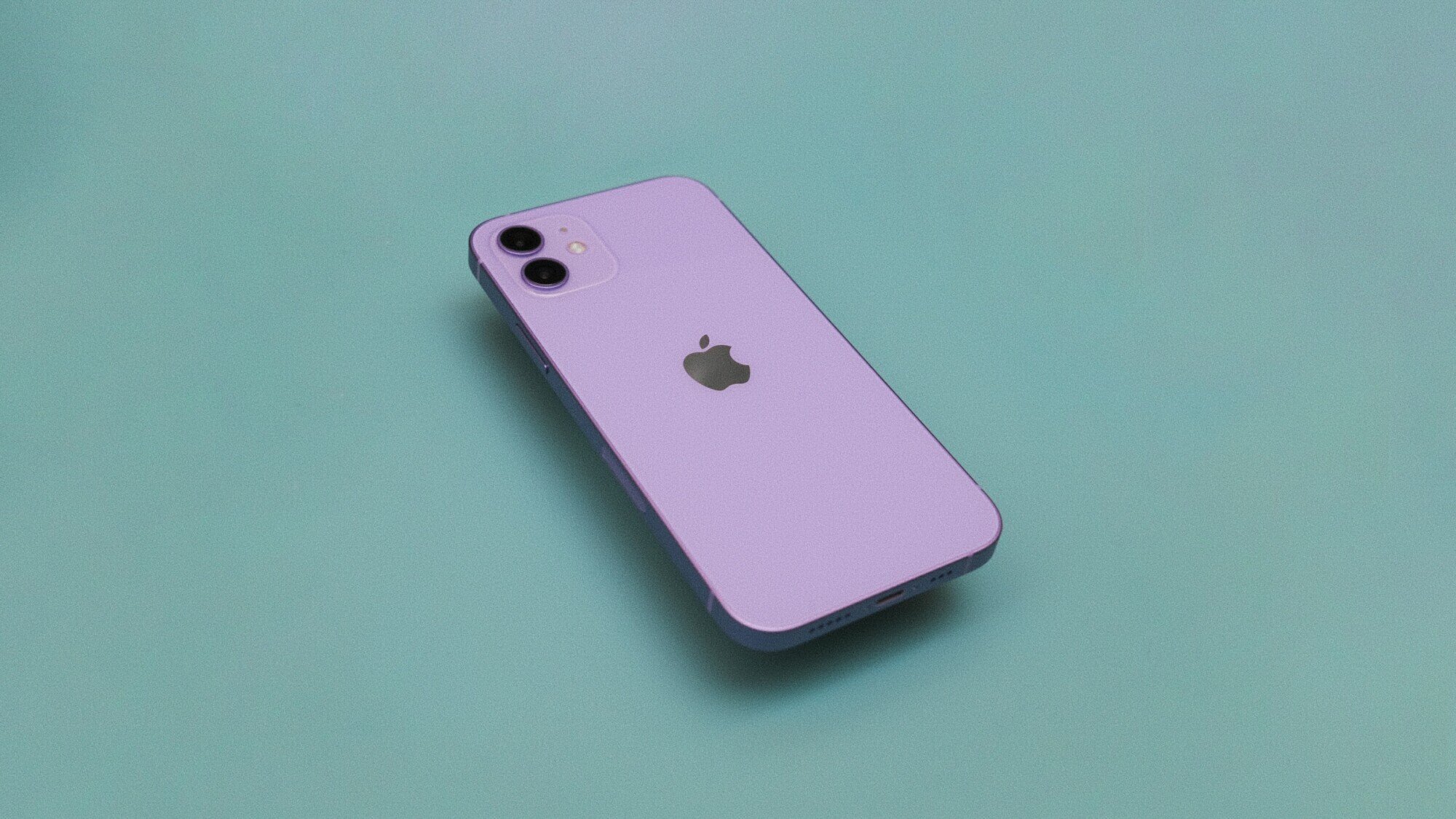 Light purple iPhone 12 lays face down on a green surface.