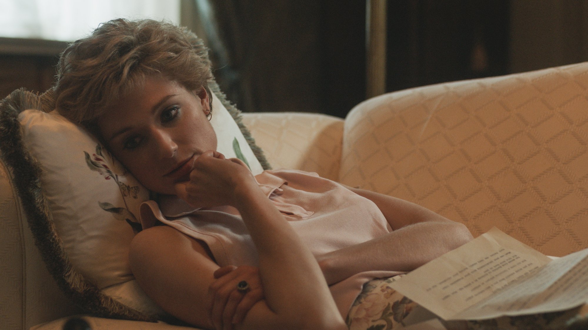 Princess Diana lies on the couch with pages of something in her lap in "The Crown."