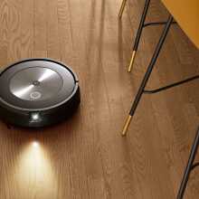 Roomba j7 robot vacuum cleaning hardwood floor with kitchen chair legs in peripherals