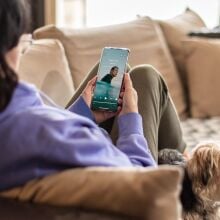 a person sits on a couch while looking at the calm app on a smartphone. A small dog is also lounging on the couch