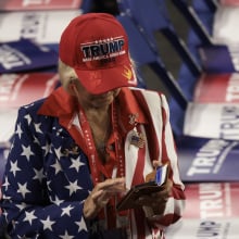 a woman in a trump hat scrolling on her phone, surrounded by trump signs