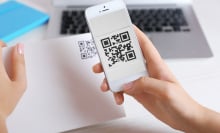 QR code on a piece of paper with person scanning it on their phone