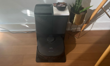 Eufy X10 Pro Omni robot vacuum and dock sitting on hardwood floor against will with potted plant and desk in peripherals