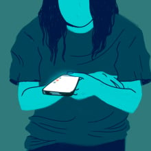 A woman looks down at her phone, against a blank background. 